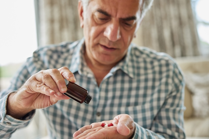 Mature Man Sitting On Sofa At Home Taking Medication Pills From Bottle